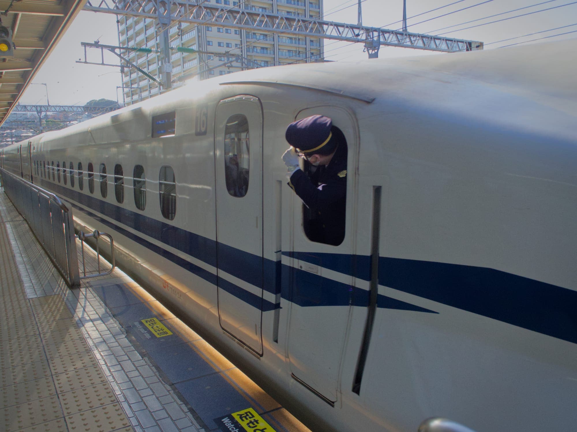 Shinkansen conductor holding onto his cap as he speeds away