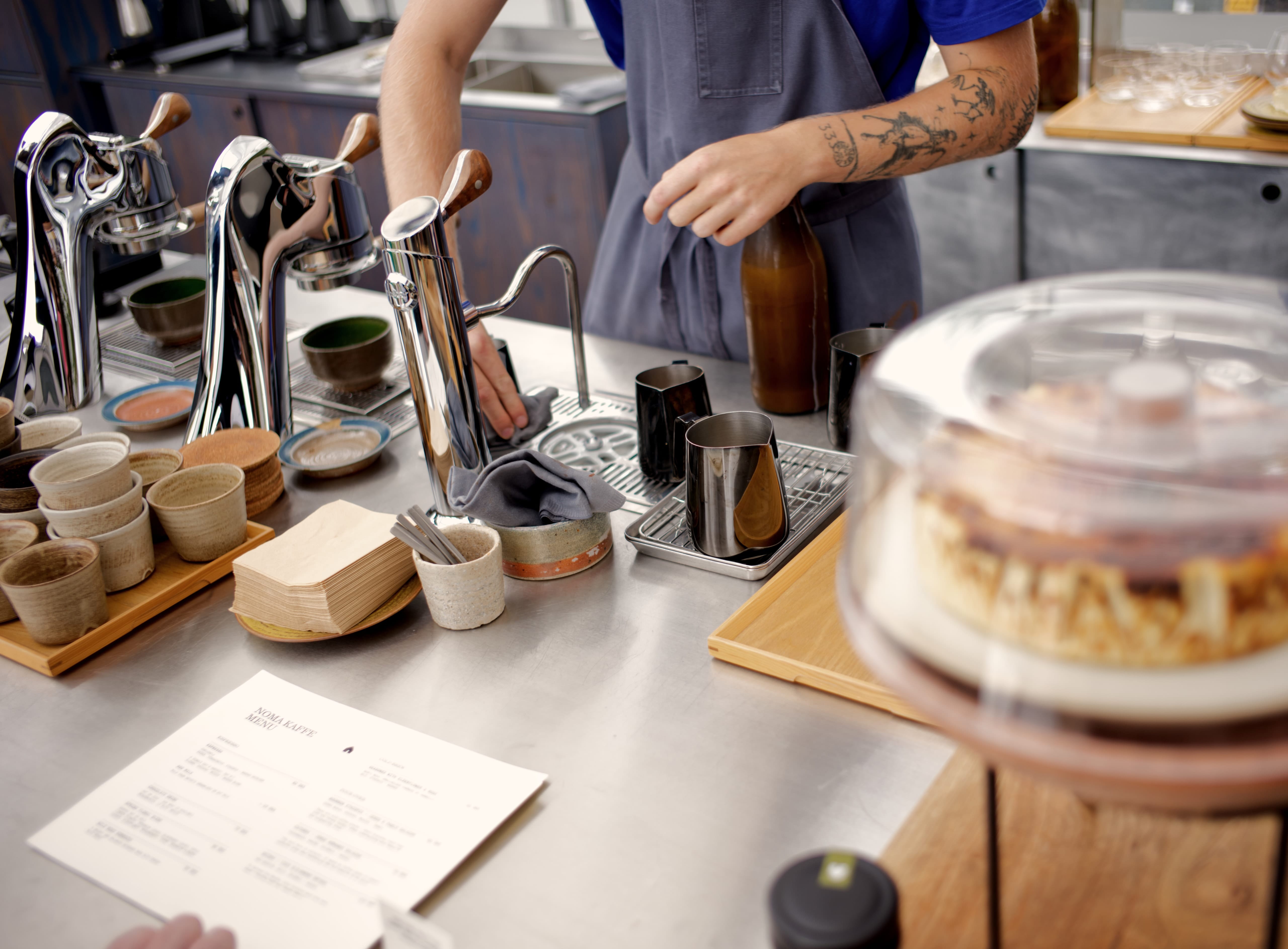A barista preparing coffee among polished metal pots and handmade cups