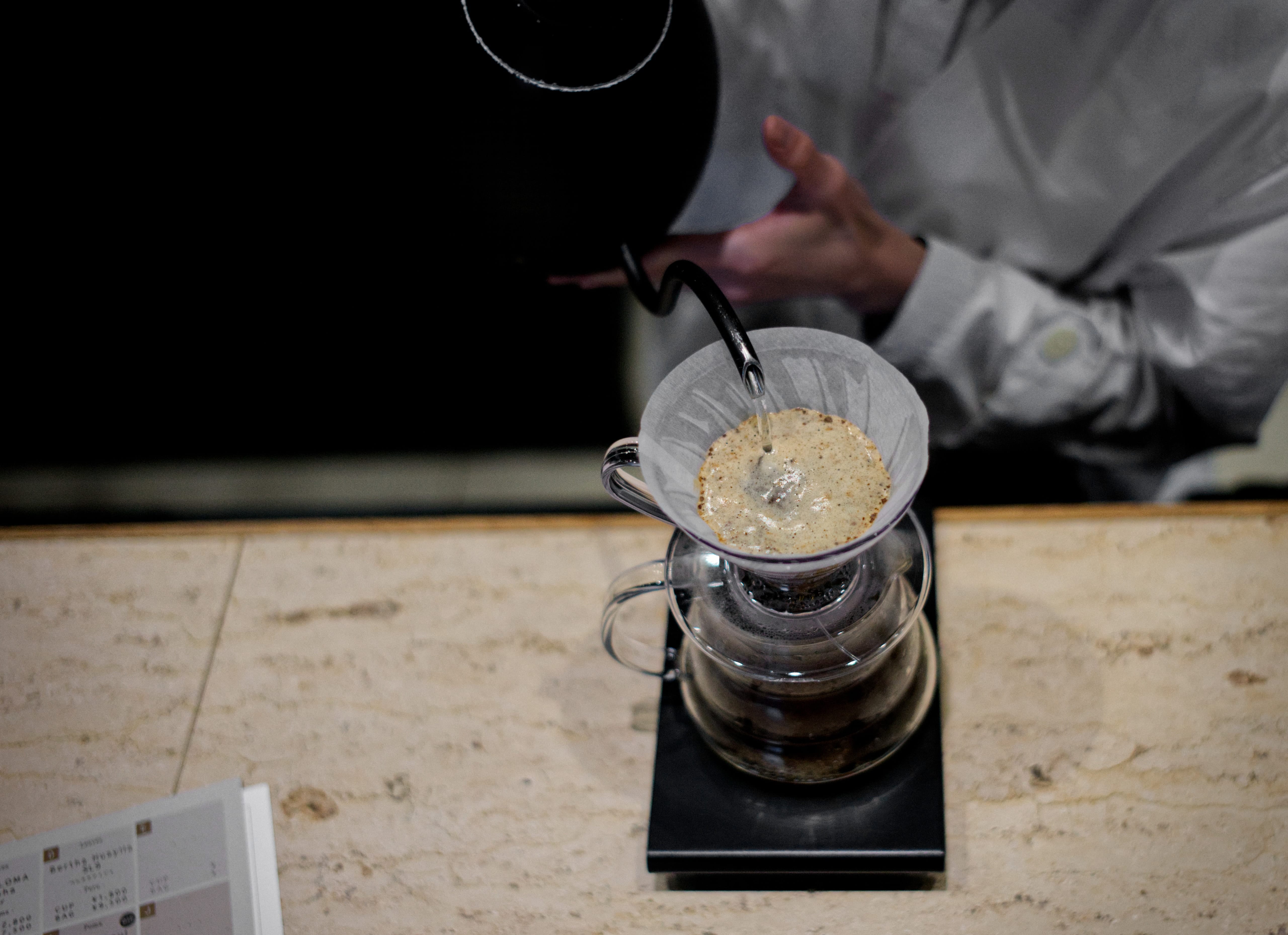 A barista pouring water into a glass coffee dripper at Koffee Mameya Kakeru