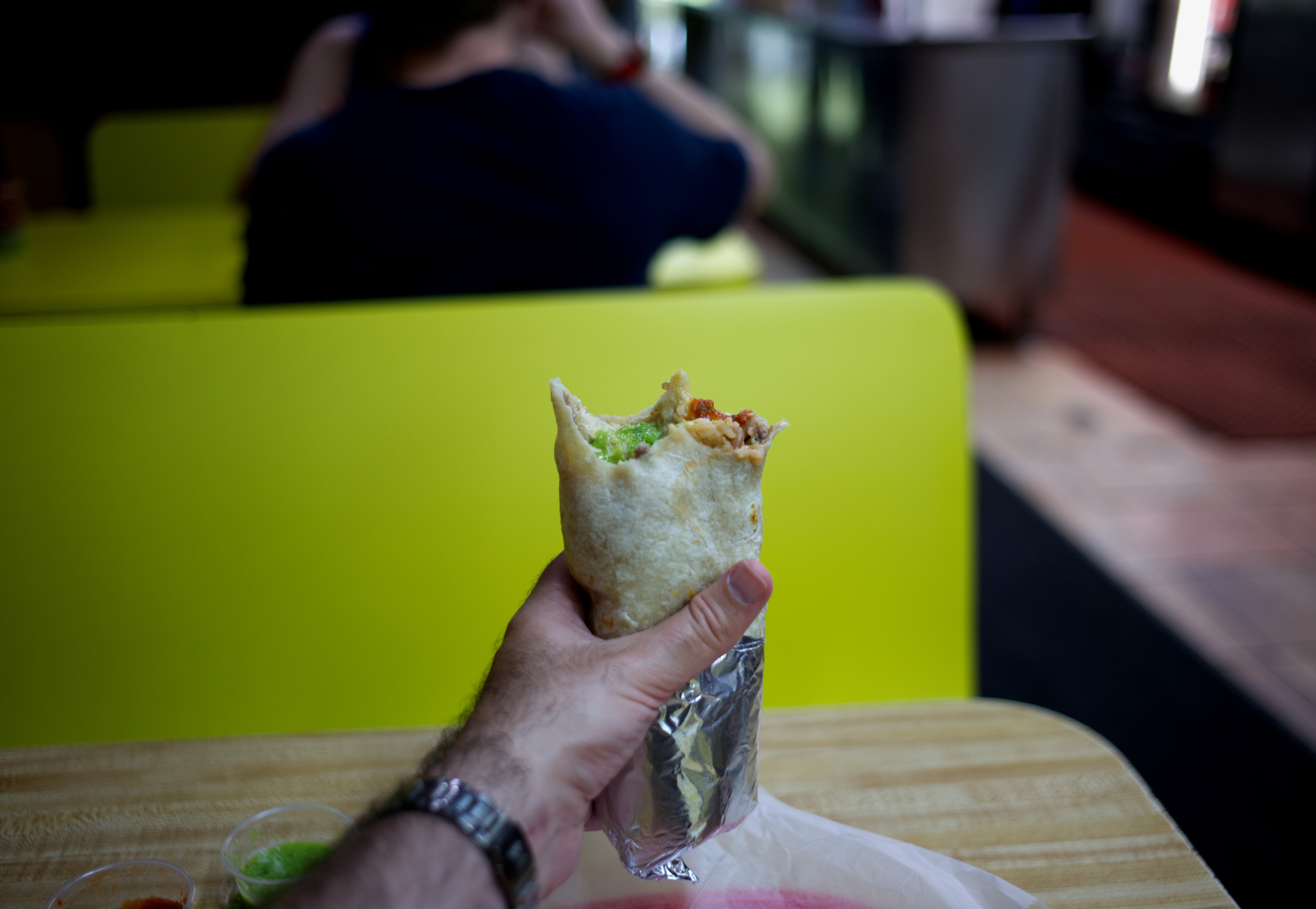 A hand holding a partially eaten foil-wrapped burrito inside Taquería El Farolito