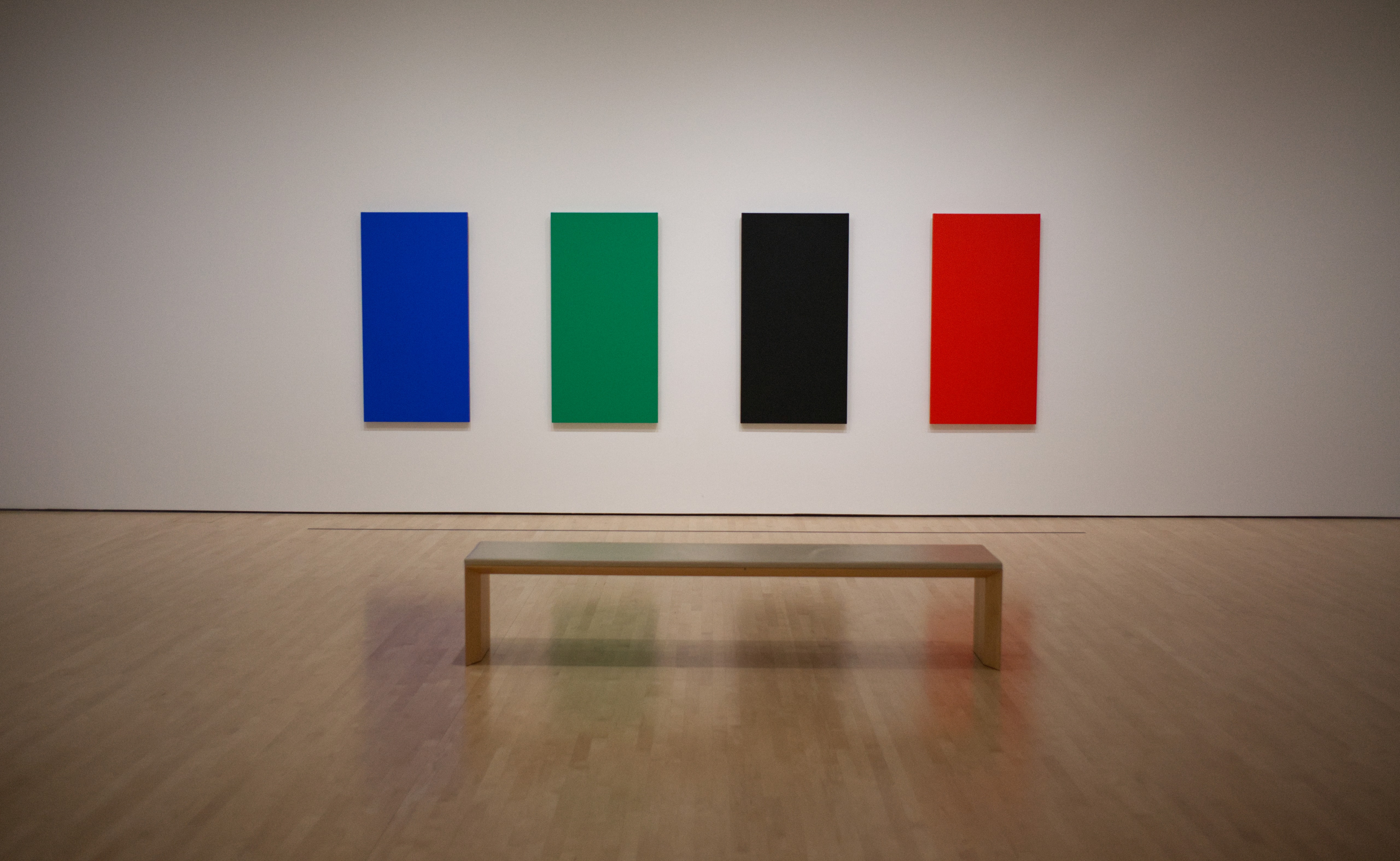 Four blue, green, black, and red rectangular artworks hanging above a bench at SFMOMA