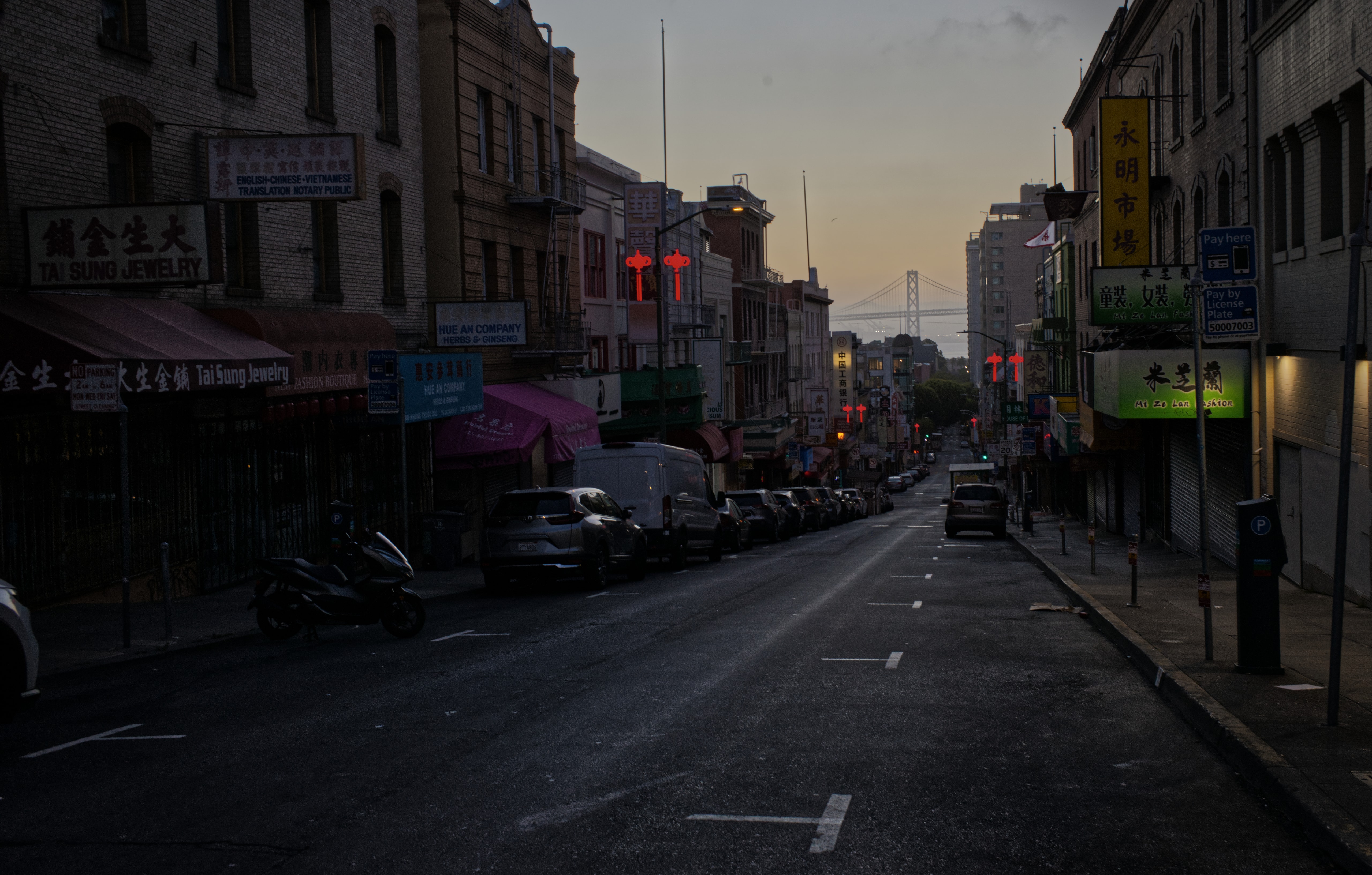 Chinatown storefronts and red lanterns at sunrise, with the Bay Bridge in the distance