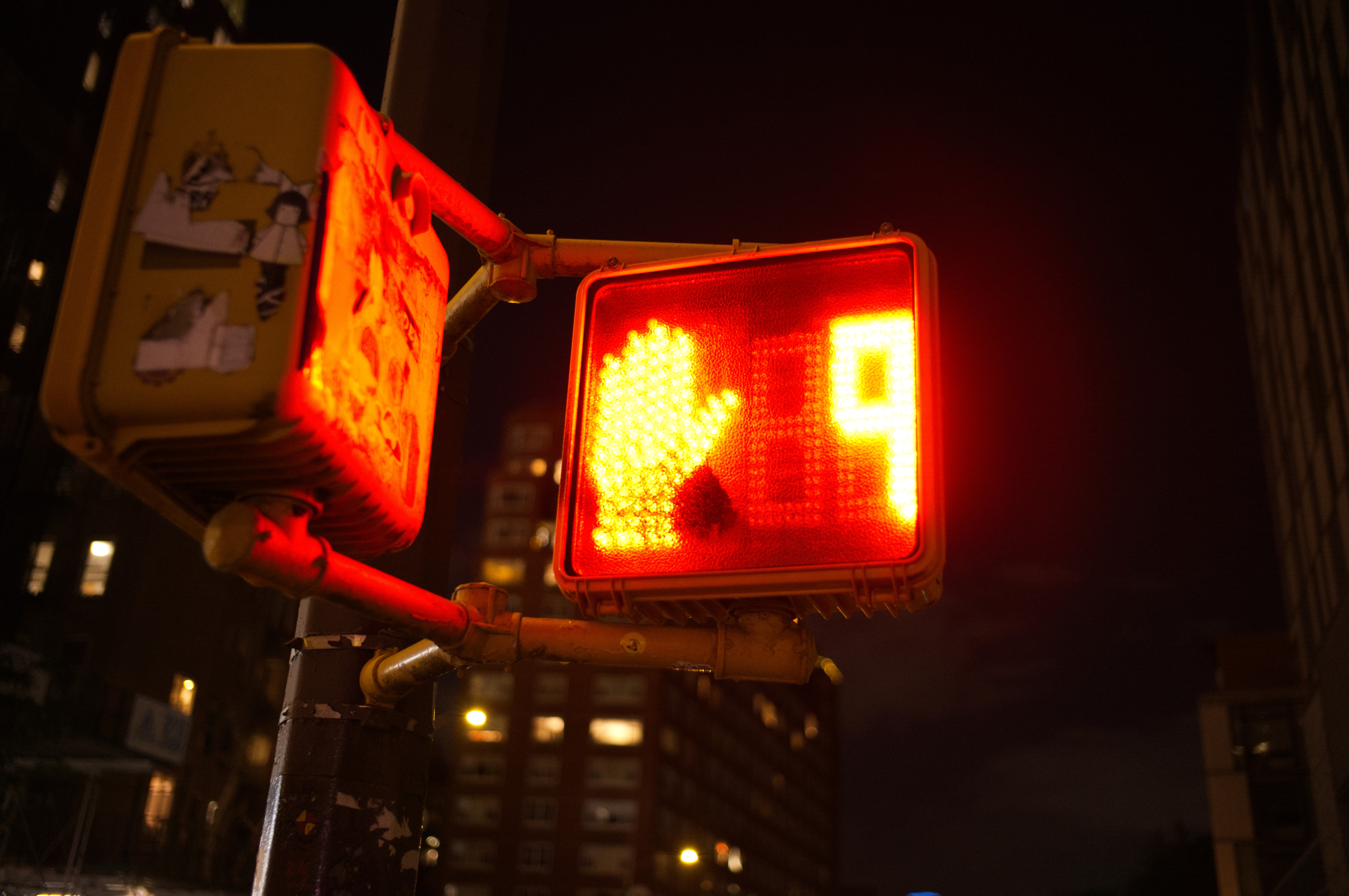 A glowing red hand on a pedestrian signal viewed from below at night