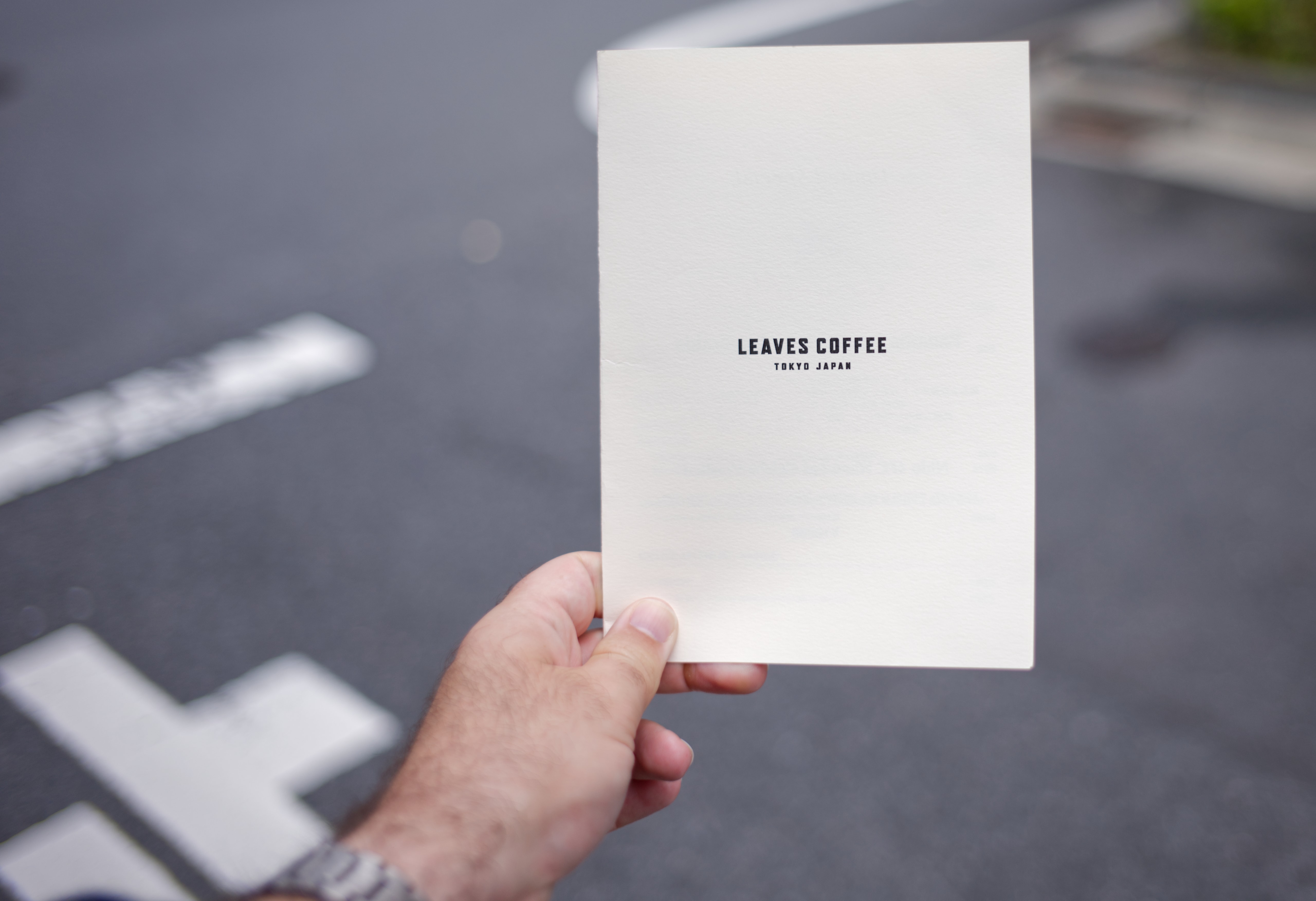 A hand holding a Leaves Coffee card outside on a Tokyo street